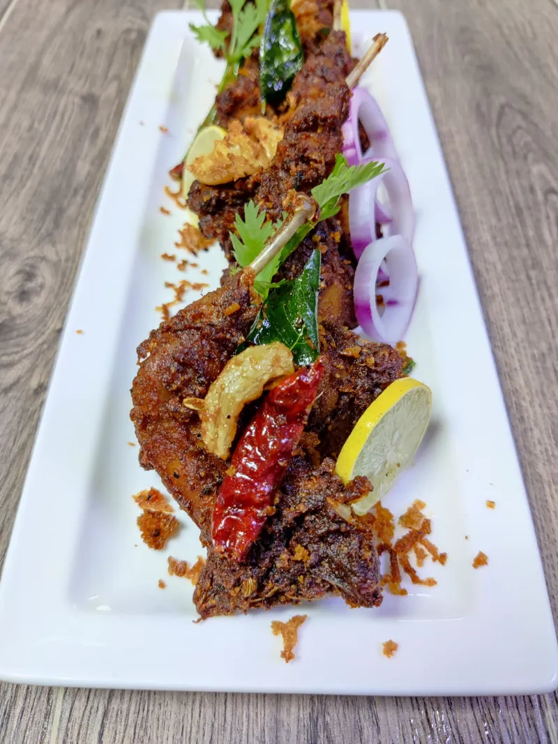 Plated spiced meat with onion rings, lemon and curry leaf